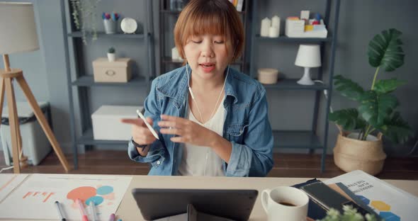Asia businesswoman using tablet talk to colleagues about plan in video call while working from house