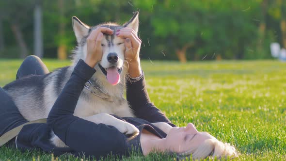 Beautiful Young Woman Playing with Funny Husky Dog Outdoors in Park alt