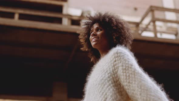 Smiling Young Woman With Windswept Afro Hair Walking Along Street alt