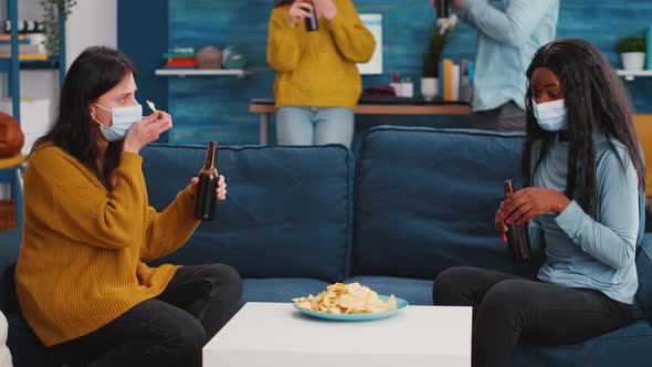 Women Sitting on Sofa Discussing Taking Off Protective Mask Eating Snacks alt