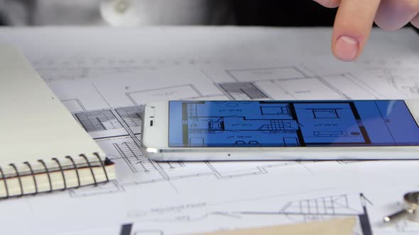 Engineer Looks at the Drawings and Graphics in the Phone. Close Up alt