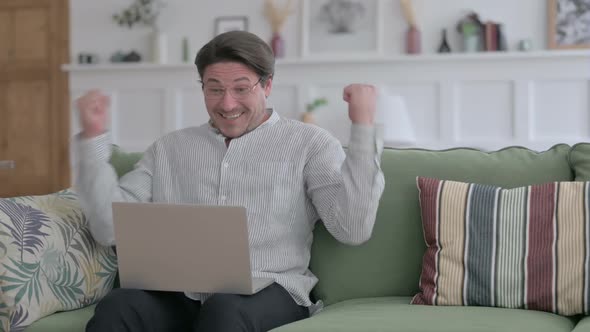 Young Man with Laptop Celebrating Success on Sofa alt