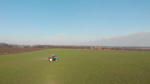 Tractor Spreading Artificial Fertilizers in Green Field. Farmer Fertilizing Arable Land with alt
