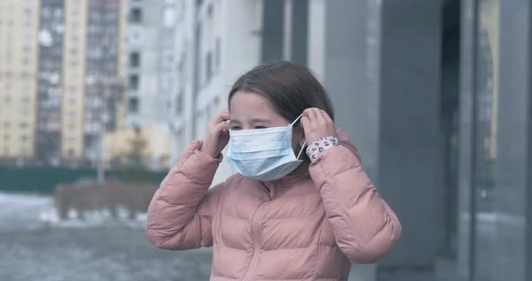 Coronavirus Protection. A Caucasian Girl Puts on a Medical Protective Mask Standing on a Street