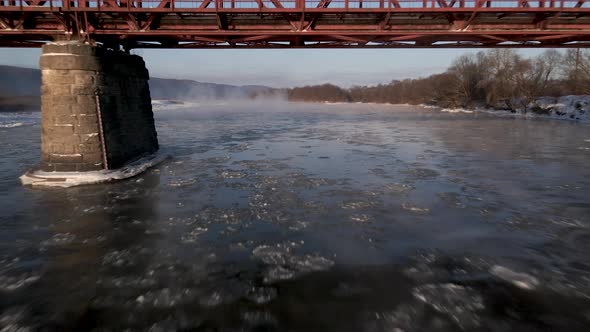 Drone Shot Flies Forward Over the Frozen River and Under the Red Steel Bridge Aerial  Footage