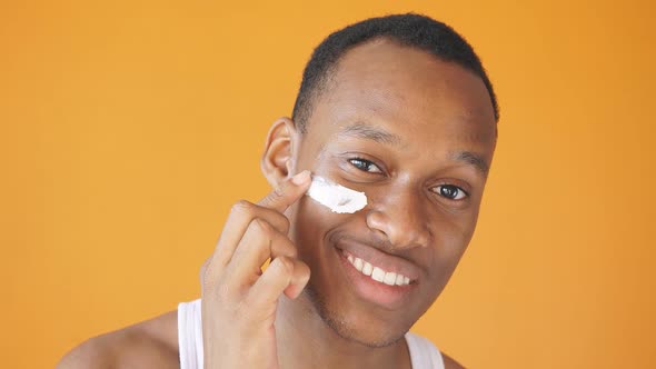 AfricanAmerican Man Applies a White Mask to His Face for Healthy Glowing Skin on an Isolated Yellow