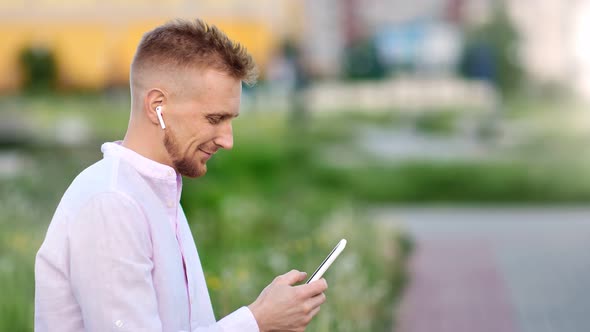 Happy Young Handsome Man Listening Music Wearing Wireless Earphones Using Smartphone alt