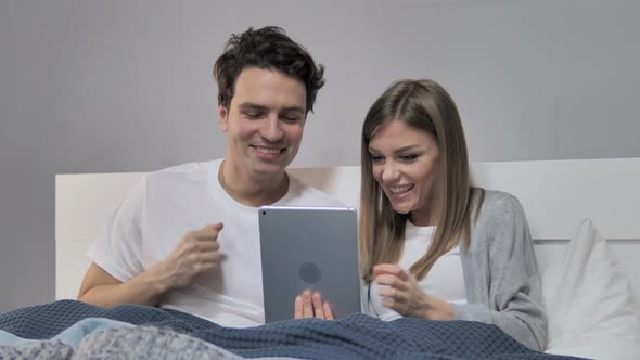 Young Couple Cheering for Win while Using Tablet in Bed alt