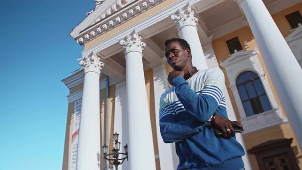 A Young Black Student with Headphones Walks Through the City Centre at Sunset