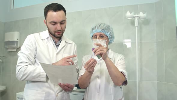 Male Doctor Talking To Nurse Holding Blood Sample alt