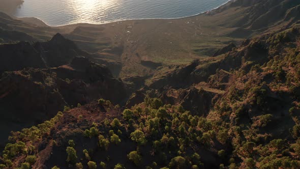 Aerial dolly tilt down over sunlit caldera Las Playas of ocean coast alt