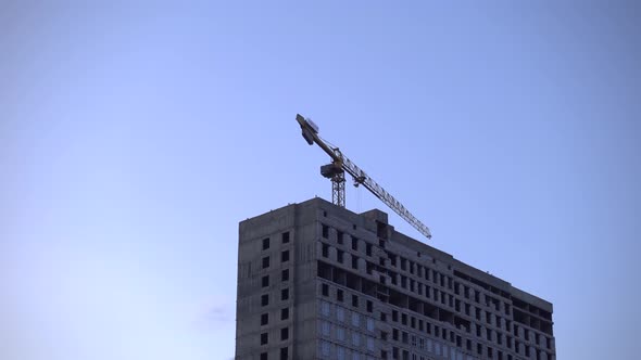 A Construction Crane Transports Cargo. Sunset in City. Construction of a Multi-storey Building.