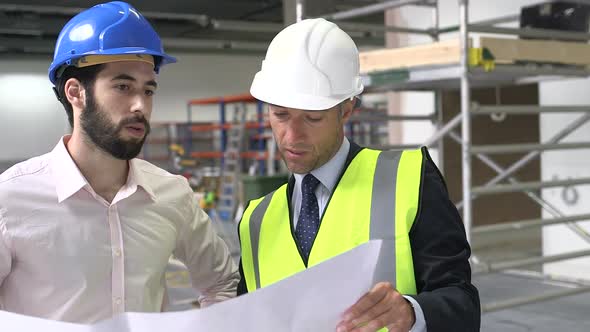 Male architect discussing with blueprint at construction site