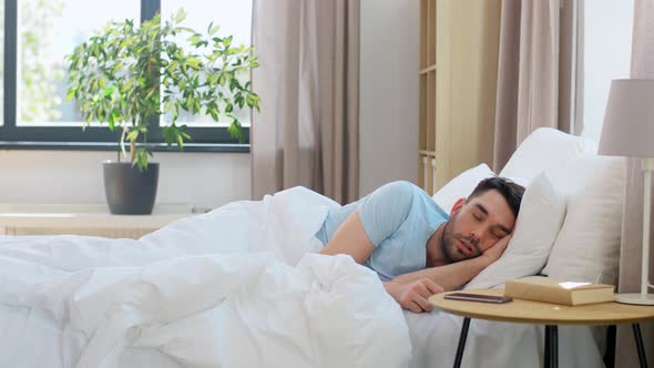 Man Sleeping in Bed Checking Time on Smartphone