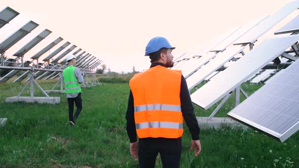 Two Old Construction Engineers Walk Between the Solar Panels on the Ecological Station. alt