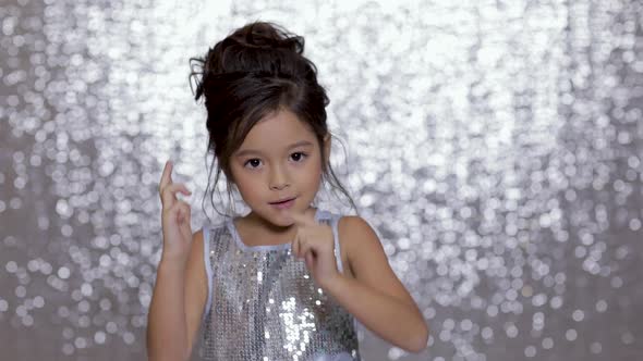 Cute Happy Little Girl Child in a Silver Dress Dancing on Background of Silver Bokeh.