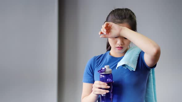 Medium Closeup Portrait of Smiling Asian Woman Tired After Workout Drinking Water From Bottle alt