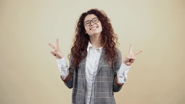The Cheerful Young Woman with Her Teeth Out Shows the Gesture of Peace with Both Hands alt