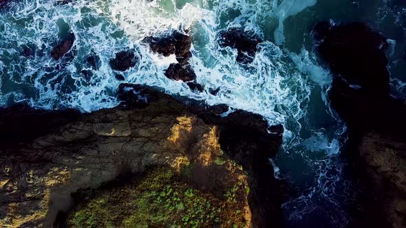 Rising aerial shot of waves crashing into a rocky cove on the California coast alt