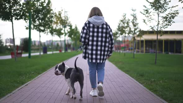 Back View Young Caucasian Woman in Eyeglasses Strolling with Dog Turning Laughing alt