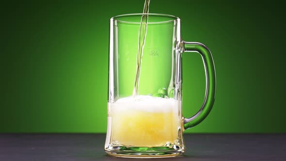 Beer Slowly Pours Into a Glass on Green Background alt