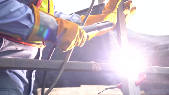 Professional welder welds a metal frame with a welding machine with fire spark in factory. alt