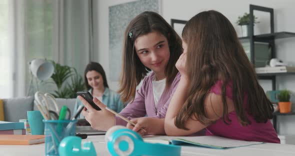 Young girls sitting at desk at home and connecting to social media using a smartphone