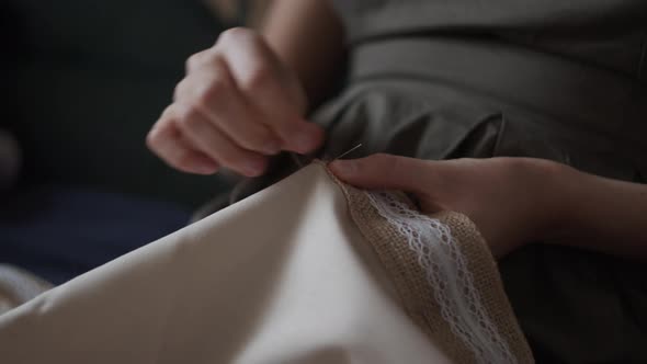 Closeup view of female hands sewing  jute linen stripe to beige cotton cloth. Boho rustic home decor alt