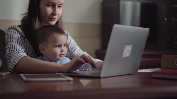 Portrait of Mother and Little Son Seated with a Laptop at the Table Indoors alt