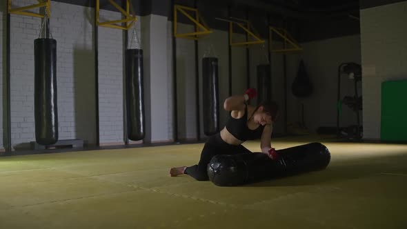 Kickboxing Aggressive Woman Fighter Trains His Punches Beats a Punching Bag While Lying on the Floor alt
