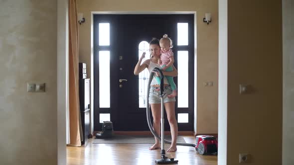 young mother vacuuming the floor in the hallway of the house with a small child alt
