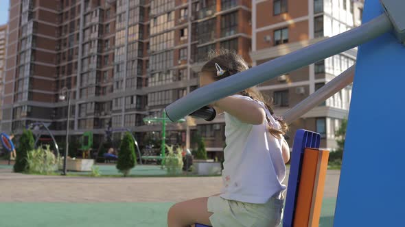 Little Adorable 5Yearold Girl is Engaged on Sport Simulator on the Street Playground in the Sunset