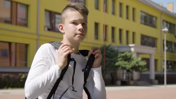 A Caucasian Teenage Boy Smiles at the Camera  a School in the Background