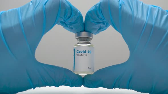 Heart-shaped hands in blue medical gloves holding a dose of coronavirus vaccine in a glass bottle