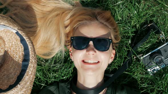 beautiful blond girl lies on the grass and fools around. takes off and puts on a hat lying on the gr alt