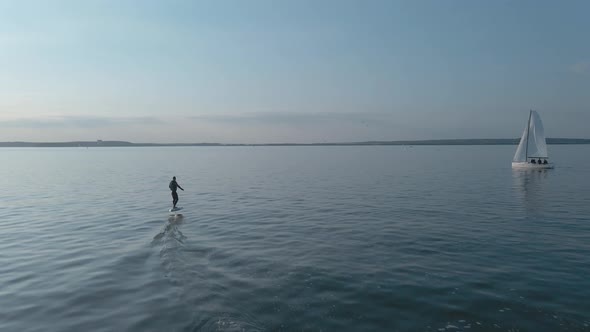 Man Riding on a Hydrofoil Surfboard on Large Blue Lake in Sunny Weather alt
