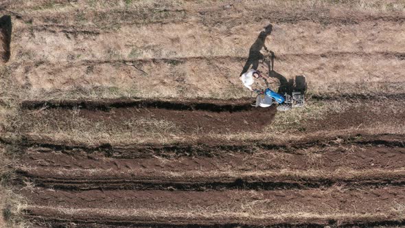 AERIAL - Man working a field with a rototiller, agriculture in Sweden, wide shot alt