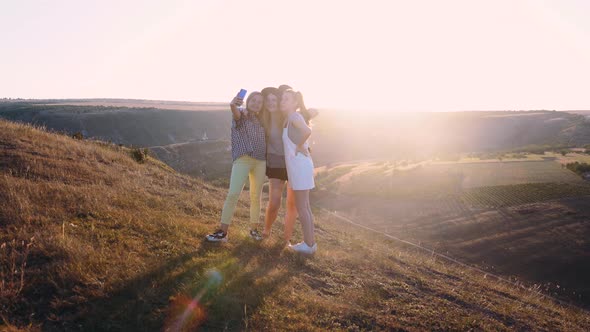 A Group of Three Girls Filming a Video Blog Sitting on a Cliff in the Mountains alt