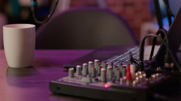 Selective Focus on Laptop Keyboard and Knobs of Audio Mixer on Podcasting Desk alt