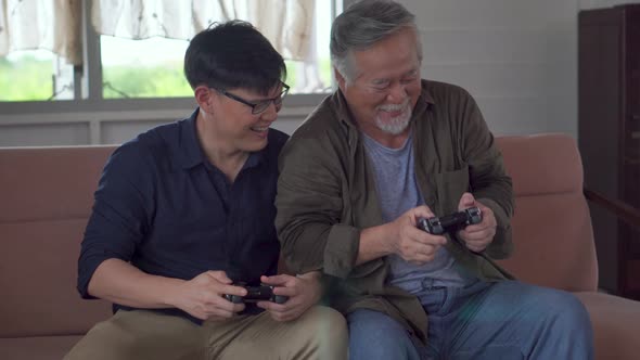 Cheerful senior Asian father and middle aged son playing video game together in living room
