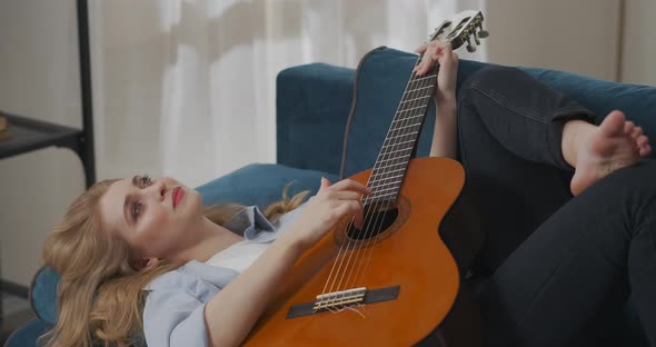 Romantic Mood of Female Musician Playing Guitar Woman Is Lying on Couch and Relaxing at Weekend alt