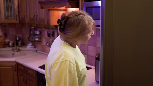 Eating disorder, hungry middle aged woman opens a refrigerator at night and eating unhealthy food. alt