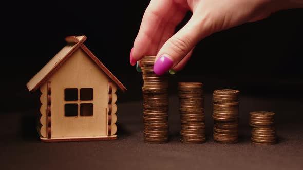 Small Wooden House with Columns of Coins on Black Background alt