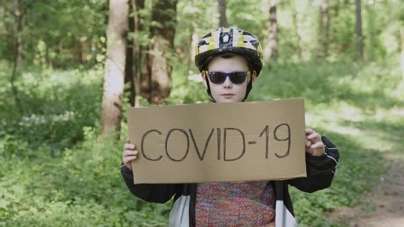 Boy in Sunglasses Helmet Turns Over Cardboard Sign with Monkeypox and Covid19 alt
