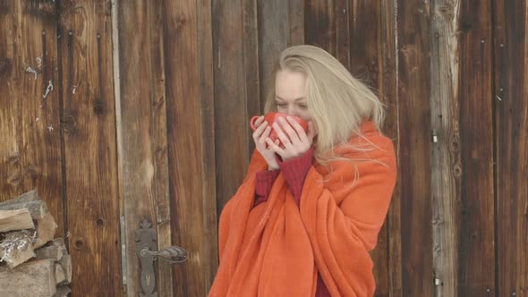 Young woman standing outside chalet and enjoying coffee during winter