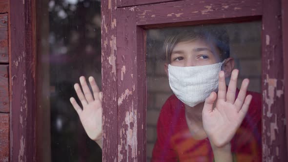 Boy in Medical Mask Inside Looks at the Window Takes Off the Mask