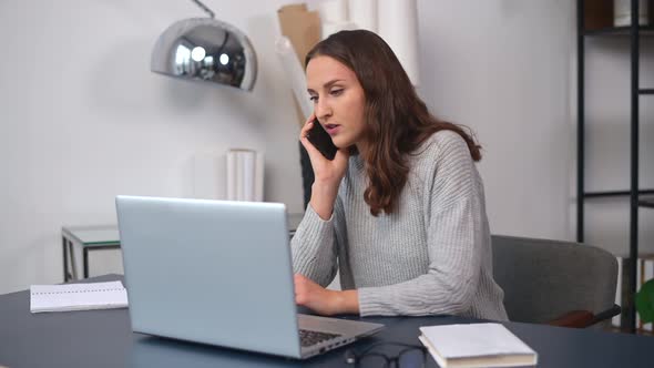 Positive Young Female Entrepreneur in Casual Wear Talking on the Smartphone alt
