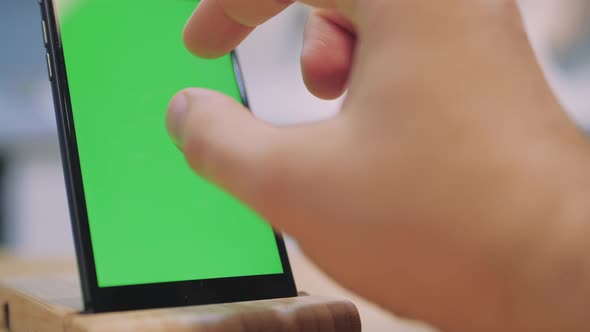 Man Touches and Looks at the Screen of the Black Smartphone with a Green Screen. Close Up alt