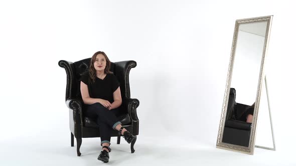 Young Woman Talking Presenting Something in Black Sofa Over White Studio