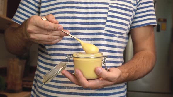 Man scooping and pouring peanut butter. Creamy smooth peanut butter in a glass jar